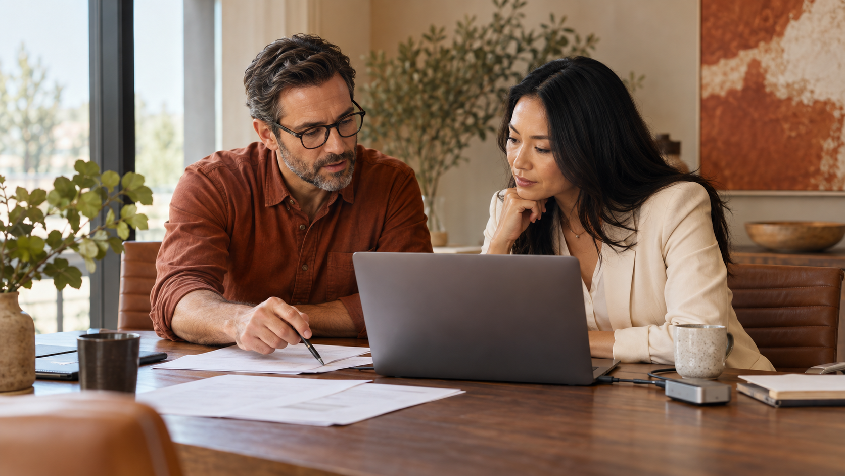 Two marketers reviewing connected data on a laptop at a warm wooden conference table.